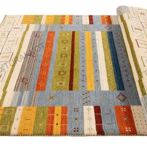 May include: A rectangular area rug with a geometric design. The rug features a light blue central field with vertical stripes in various colors, including orange, green, and yellow. The border has a cream background with repeating square patterns.