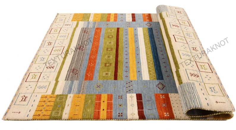 May include: A rectangular area rug with a geometric design. The rug features a light blue central field with vertical stripes in various colors, including orange, green, and yellow. The border has a cream background with repeating square patterns.