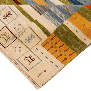 May include: A colorful, geometric area rug with a folded corner. The rug features a cream-colored background with squares and rectangles in shades of blue, green, orange, and brown. The design includes stylized patterns and shapes.