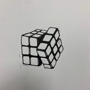 May include: A black and white linocut print depicting a Rubik's Cube. The cube is partially solved, with some faces aligned and others scrambled. The print is on a white background.