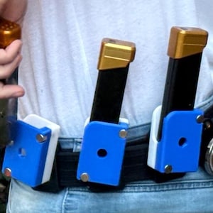 May include: A black belt with three blue and white magazine holders. Each holder has a black magazine with a gold top. The person is wearing a white shirt and blue jeans.