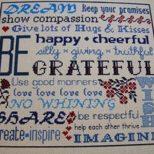 May include: Cross-stitch embroidery with a white background and blue and red lettering. The text reads "DREAM Keep your promises show compassion Give lots of Hugs & Kisses happy cheerful silly giving truthful BE GRATEFUL Use good manners love love love love NO WHINING SHARE be respectful create-inspire help each other thrive IMAGINE".