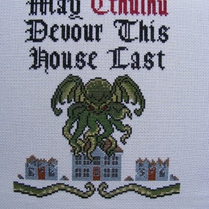 Könnte beinhalten: Kreuzstich-Stickerei mit einem grünen und schwarzen Cthulhu-Monster mit Tentakeln, das auf einem blauen Haus steht, mit zwei kleineren Häusern auf beiden Seiten. Der Text "May Cthulhu Devour This House Last" ist in Schwarz und Rot gestickt.