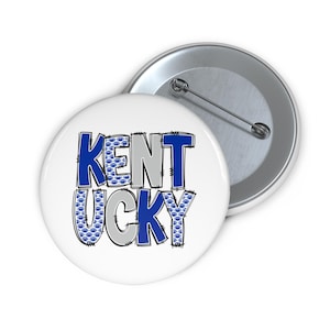 Puede incluir: Botón blanco con la palabra "KENTUCKY" en letras de bloque azules y grises. Las letras están delineadas en negro. La letra "E" en "KENT" y la letra "U" en "UCKY" están rellenas con un patrón de huellas de patas azules.