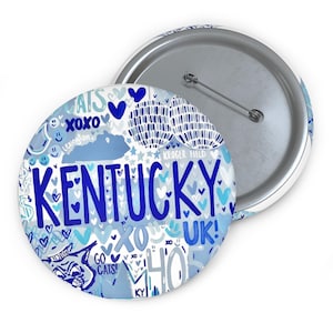 May include: A round button with a silver metal back and pin. The front of the button is white and light blue, with the word "Kentucky" in large blue letters. The button has various other blue text and graphics.