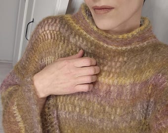 Puede incluir: Un suéter calado multicolor en tonos amarillos, lavanda y marrón. El suéter tiene un cuello alto acanalado y mangas largas. La prenda de punto parece suave y ligera, adecuada para usar en capas. El estilo general es informal y cómodo.