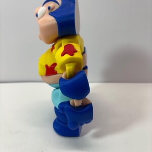 K&ouml;nnte beinhalten: 3D-gedruckte Actionfigur einer Zeichentrickfigur. Die Figur hat einen blauen Helm, einen gelben Torso und blaue Stiefel. Rote Akzente befinden sich auf den Schultern und der Brust. Die Figur steht auf einer wei&szlig;en Oberfl&auml;che.