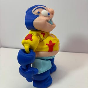 K&ouml;nnte beinhalten: Eine 3D-gedruckte Figur einer Zeichentrickfigur. Die Figur hat einen blauen Helm, eine gelbe Jacke mit roten Sternakzenten und blaue Handschuhe und Stiefel. Die Figur hat eine gro&szlig;e Nase und einen offenen Mund.
