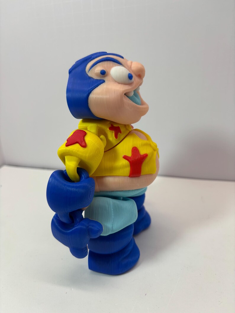 K&ouml;nnte beinhalten: Eine 3D-gedruckte Figur einer Zeichentrickfigur. Die Figur hat einen blauen Helm, eine gelbe Jacke mit roten Sternakzenten und blaue Handschuhe und Stiefel. Die Figur hat eine gro&szlig;e Nase und einen offenen Mund.