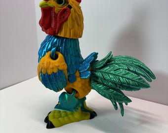 May include: A colorful, decorative rooster figurine. The rooster features a red comb, yellow head and body, blue accents, and green tail feathers. The figurine is made of a hard material and has a detailed design.