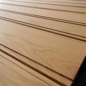 May include: Close-up of light brown wooden planks with a grooved design. The planks are arranged diagonally, showcasing the wood grain and the recessed grooves that run parallel to each other. The wood has a natural, warm tone.