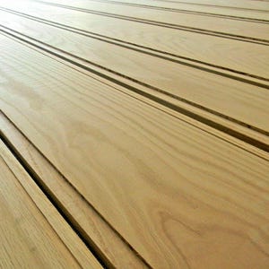 May include: Close-up of several light-colored wooden planks with dark grooves. The planks are arranged diagonally, creating a sense of depth and texture. The wood grain is visible, adding to the natural aesthetic. The image showcases a carpentry or woodworking theme.