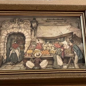 May include: Framed relief sculpture depicting a bustling outdoor market scene. The artwork features a variety of fruits and vegetables displayed on wooden tables, with figures of people interacting. The frame is a warm brown color.