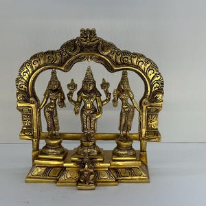 May include: A golden-colored, ornate statue featuring three figures within an arched frame. The figures stand on individual pedestals, and the entire piece is richly detailed with intricate carvings. The statue is likely a religious or cultural artifact.