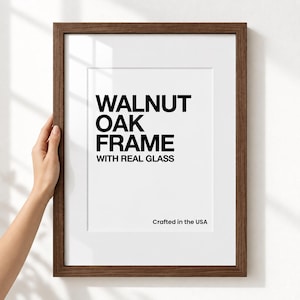 May include: A rectangular dark brown wooden picture frame with a white mat board. The center text reads WALNUT OAK FRAME WITH REAL GLASS and the bottom right corner text reads Crafted in the USA. The frame has a clean, simple design.