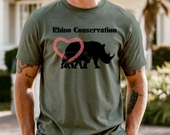 Puede incluir: Camiseta verde oliva con el texto "Rhino Conservation" sobre una silueta de rinoceronte negro y un corazón rosa. La camiseta es de manga corta y tiene cuello redondo.