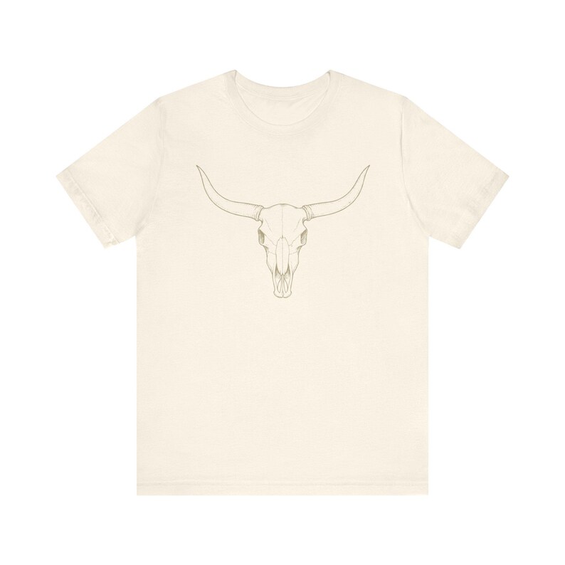 Puede incluir: Camiseta color crema con un dibujo lineal detallado de una calavera de toro. La calavera tiene cuernos largos y curvados y est&aacute; centrada en la parte delantera. El dise&ntilde;o es en un tono neutro y terroso, creando una est&eacute;tica minimalista.