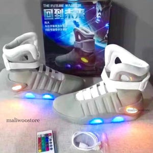 May include: Gray and white futuristic sneakers with blue and orange LED lights. The sneakers have a high-top design with a strap and a box in the background with the text "THE FUTURE WARRIOR" and Chinese characters.