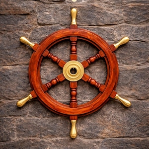 May include: A wooden ship's wheel with a rich, dark brown finish and brass accents. The wheel has six spokes and a central brass hub. The handles are also brass. The wheel is mounted on a textured, gray stone wall.