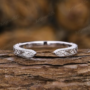 May include: A silver-toned open band ring featuring an intricate engraved scrollwork pattern along the outer surface. The ring has a gap at the front, creating a horseshoe-like shape with detailed metalwork extending from the ends to the sides.