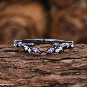 May include: A black ring with leaf-like designs, adorned with purple and white gemstones. The ring features the text "ArtjewelUS" in the background. The gemstones are set in a delicate pattern, creating an elegant and eye-catching piece of jewelry.