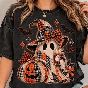 Peut inclure: Un t-shirt gris anthracite avec un motif représentant un fantôme portant un chapeau de sorcière en patchwork avec un nœud à carreaux. Le fantôme tient un gobelet en plastique avec une paille à côté d'une citrouille à carreaux et des chauves-souris.