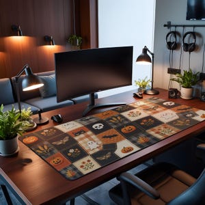 May include: A rectangular desk mat featuring a patchwork design with Halloween-themed illustrations including pumpkins, ghosts, skulls, black cats, moths, and autumn leaves in shades of orange, black, white, and grey on a wooden desk surface.