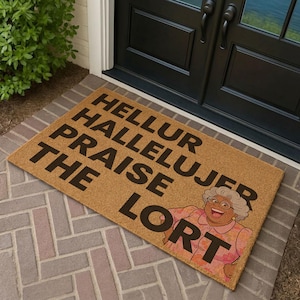 May include: A rectangular tan coir doormat featuring bold black text that reads HELLUR HALLELUJER PRAISE THE LORT. The mat includes a colorful illustration of an older person with gray hair, glasses, and a floral shirt, positioned on the right side.
