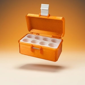 Könnte beinhalten: Eine kleine, rechteckige orangefarbene Aufbewahrungsbox mit offenem Klappdeckel und einem weißen Verschluss. Das Innere verfügt über einen weißen Einsatz mit acht kreisförmigen Fächern in zwei Viererreihen zur sicheren Aufbewahrung.
