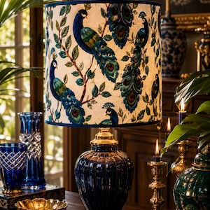 May include: A navy blue table lamp with a peacock design lampshade. The lampshade features a cream background with peacock illustrations in shades of blue and green. The lamp base is navy blue with gold accents, and other blue and gold decorative items are in the background.