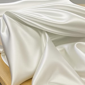Könnte beinhalten: Nahaufnahme eines fließenden, cremeweißen Satin-Stoffs. Der Stoff ist drapiert und gefaltet, wodurch weiche Schatten und Glanzlichter entstehen. Das Material hat einen subtilen Glanz, der auf eine luxuriöse Textur hindeutet. Ideal für Bekleidung, Heimdekoration oder Bastelprojekte.
