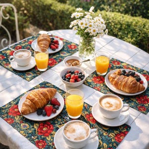 May include: A breakfast table set outdoors with croissants, berries, orange juice, and coffee. The table is covered with floral patterned placemats. A vase of white daisies sits in the center, with a garden in the background.