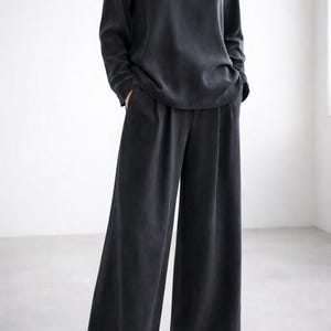 K&ouml;nnte beinhalten: Dunkelgraues Outfit, bestehend aus einem lang&auml;rmeligen Oberteil und einer Hose mit weitem Bein. Das Oberteil hat einen Rundhalsausschnitt, die Hose einen lockeren, flie&szlig;enden Schnitt. Das Outfit ist aus weichem, flie&szlig;endem Stoff gefertigt.