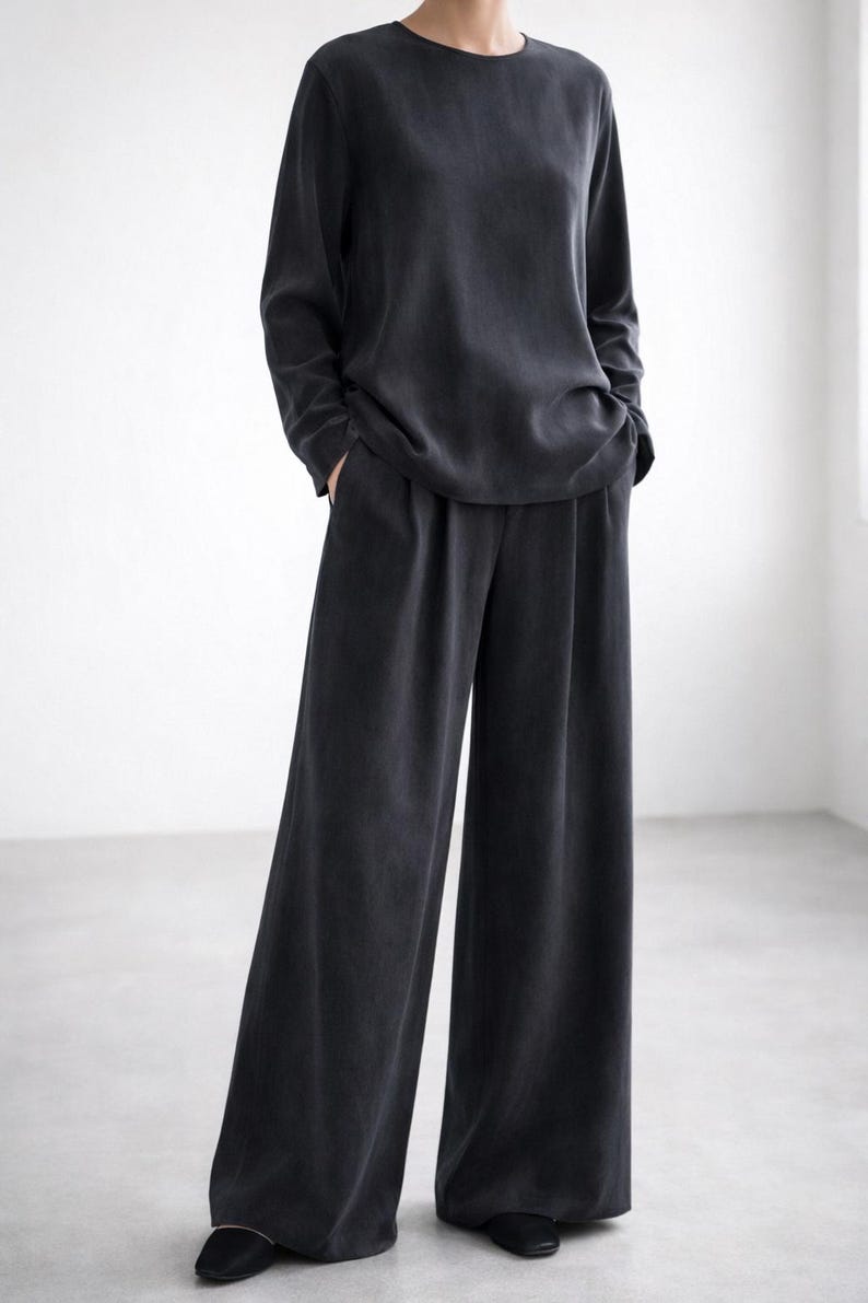 K&ouml;nnte beinhalten: Dunkelgraues Outfit, bestehend aus einem lang&auml;rmeligen Oberteil und einer Hose mit weitem Bein. Das Oberteil hat einen Rundhalsausschnitt, die Hose einen lockeren, flie&szlig;enden Schnitt. Das Outfit ist aus weichem, flie&szlig;endem Stoff gefertigt.