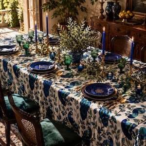 May include: A beautifully set dining table with a peacock-themed tablecloth, featuring blue and green accents. The table is adorned with blue plates, gold silverware, green glassware, and lit blue candles, creating an elegant ambiance.