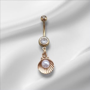 May include: Gold-colored belly button ring with a dangling seashell charm. The ring features a small, clear gemstone at the top and a larger one in the center. The seashell holds a small, white pearl.