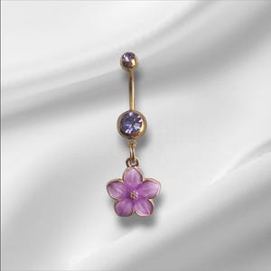 以下が含まれることがあります： 紫色の花のチャームが付いた、金色のへそピアス。リングの上部には小さな紫色の宝石、中央には大きな宝石が付いています。花のチャームは薄紫色です。