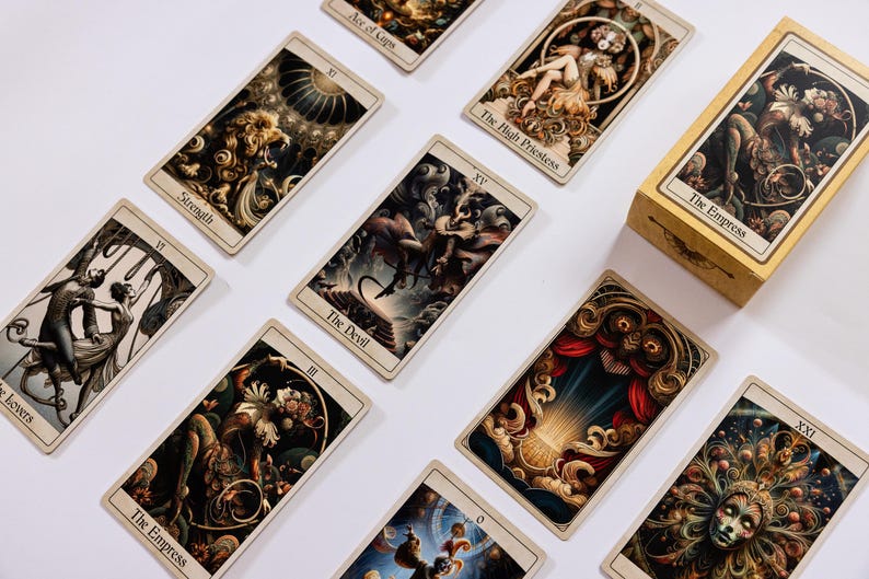 May include: A collection of tarot cards with detailed illustrations and titles like "The Empress," "The Devil," and "Strength." The cards are arranged on a white surface, with a matching box visible. The artwork features rich colors and intricate designs.