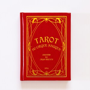 May include: A red tarot card deck titled "Tarot du Cirque Magique" with gold lettering and decorative border. The deck is created by Orlin Hristov and dated 2024. The cover has a rectangular shape.