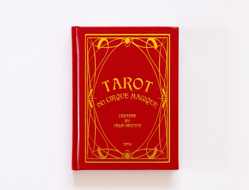 May include: A red tarot card deck titled "Tarot du Cirque Magique" with gold lettering and decorative border. The deck is created by Orlin Hristov and dated 2024. The cover has a rectangular shape.