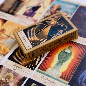 May include: A deck of Belle Epoque Tarot cards with a tan box featuring the word "Judgement". The cards have colorful illustrations with symbols and figures. The cards are spread out on a white surface.
