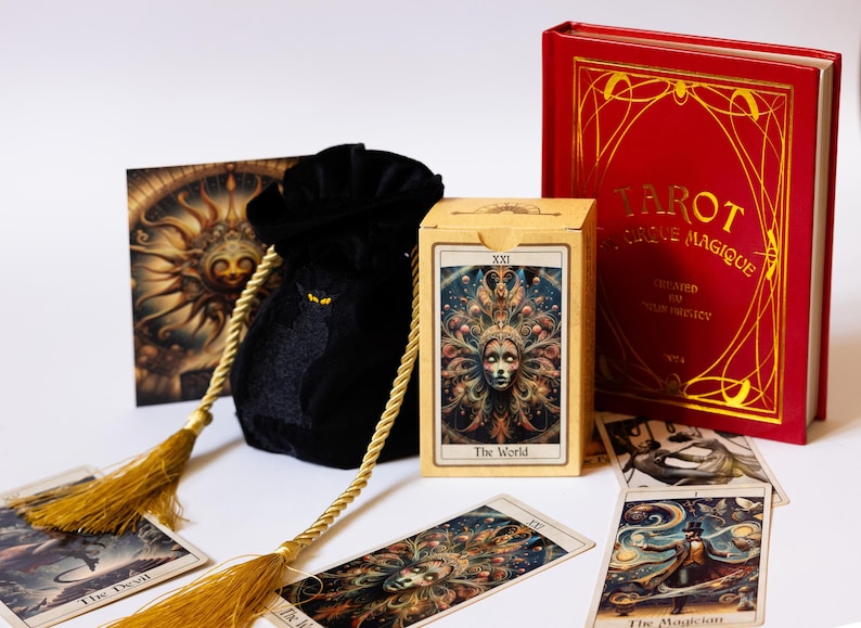 May include: A tarot card set featuring a red book with gold lettering, a black velvet bag with gold tassels, and a deck of cards. The card box displays "The World" card. Several tarot cards are scattered around the set.