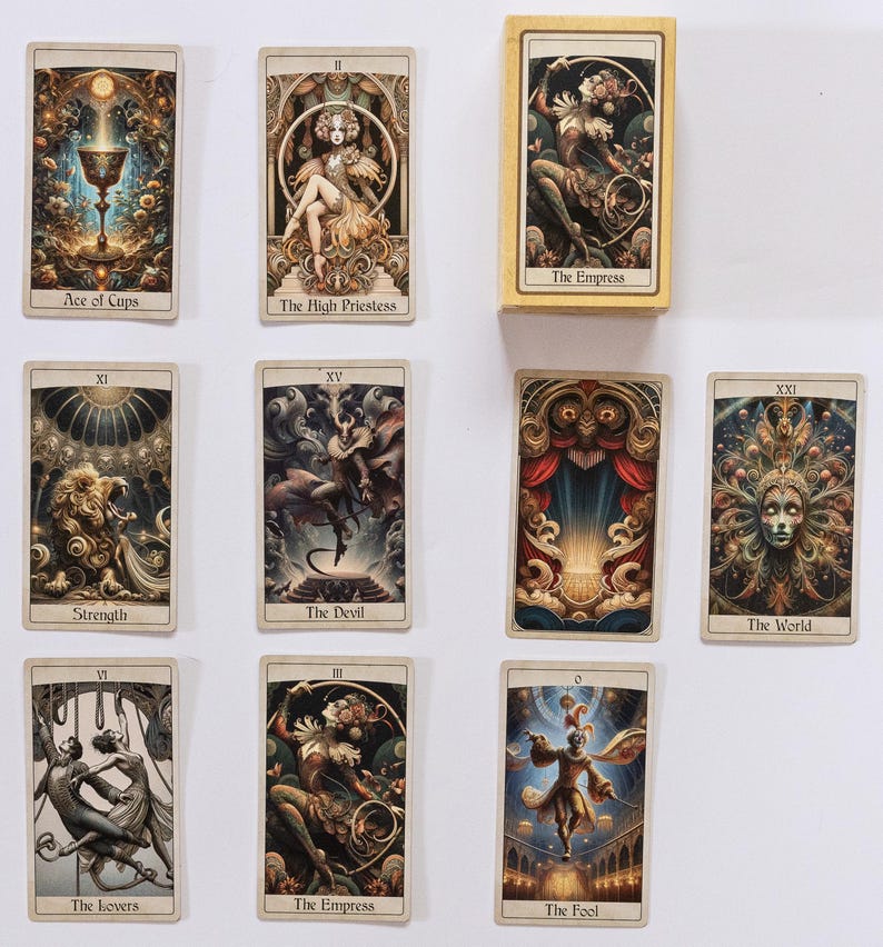 May include: A collection of tarot cards featuring intricate illustrations and text. The cards display images of "Ace of Cups", "The High Priestess", "The Empress", "Strength", "The Devil", "The World", "The Lovers", and "The Fool". The cards are in a box labeled "The Empress".