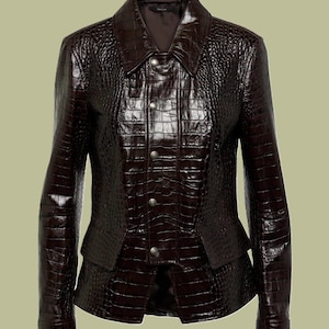 May include: A dark brown, textured leather jacket with a collared neckline and button-down front. The jacket features a tailored fit with a peplum-style waist and long sleeves. The leather has a crocodile-like embossed pattern.