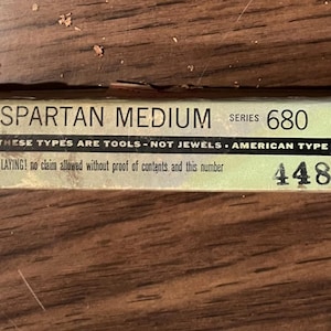 May include: A rectangular box labeled "SPARTAN MEDIUM SERIES 680" with the text "THESE TYPES ARE TOOLS - NOT JEWELS." The box is light green and beige with black text. The box also has the text "AMERICAN TYPE FOUNDERS CO., INC."