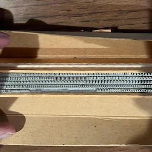 May include: A vintage wooden box containing metal letterpress type. The type is arranged in rows, with various fonts and sizes visible. The box is open, revealing the contents. The wood has a light brown color.
