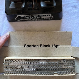 May include: A vintage Griswold Film Splicer, model 8 & 16 MM, with a metal construction. The image also shows a box of Spartan Black 18pt type, containing metal letter stamps. The text "Noumade Products Corp" is visible.