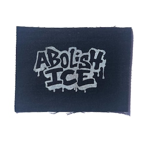Puede incluir: Un parche rectangular negro con las palabras "Abolish ICE" en una fuente estilizada y goteante. El texto es de color gris claro, contrastando con el fondo oscuro. El parche tiene un borde crudo y sin terminar.