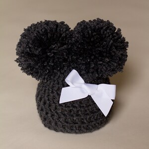 May include: Black crocheted hat with two large pom-poms on top and a white satin bow.