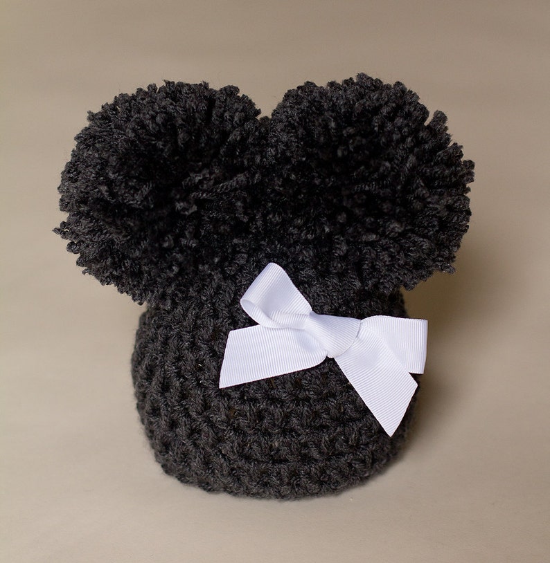 May include: Black crocheted hat with two large pom-poms on top and a white satin bow.